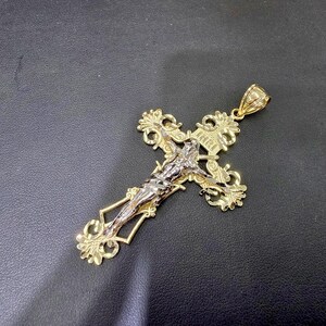 Op de afbeelding: Goudkleurige kruisbeeldhanger met een gedetailleerde Jezusfiguur in zilverkleurig metaal. Het kruis heeft sierlijke filigraanontwerpen en de inscriptie "INRI". Een religieus sieraad.