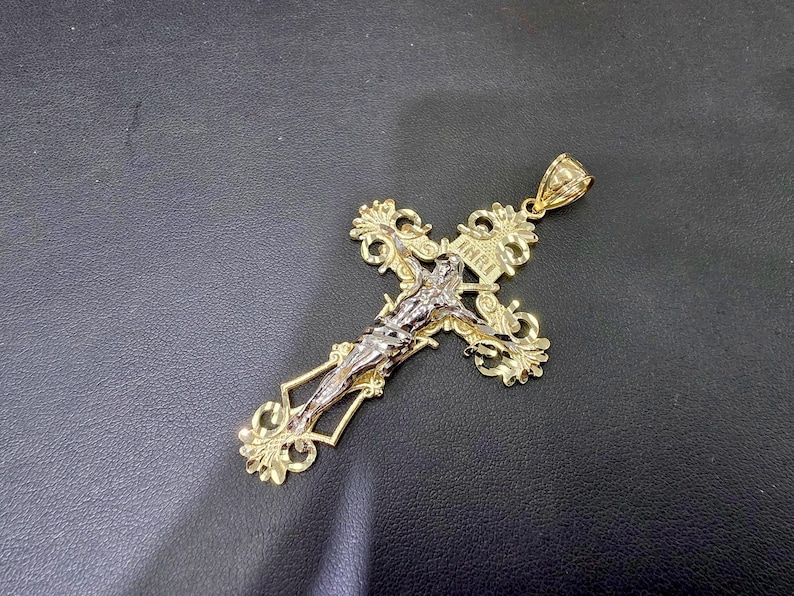 Op de afbeelding: Goudkleurige kruisbeeldhanger met een gedetailleerde Jezusfiguur in zilverkleurig metaal. Het kruis heeft sierlijke filigraanontwerpen en de inscriptie "INRI". Een religieus sieraad.