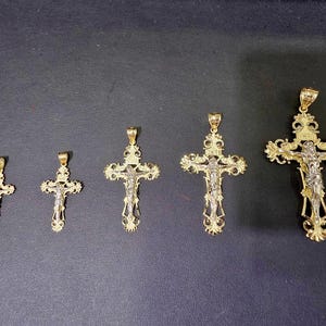 Op de afbeelding: Vijf goudkleurige kruisvormige hangers van verschillende formaten tegen een donkere achtergrond. Elk kruis heeft een gedetailleerde afbeelding van Jezus Christus en sierlijke filigraanontwerpen. Geschikt voor kettingen.