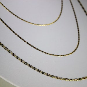 Puede incluir: Tres cadenas de oro de diferentes longitudes, todas con un dise&ntilde;o delicado y texturizado. Las cadenas est&aacute;n superpuestas sobre un fondo blanco.
