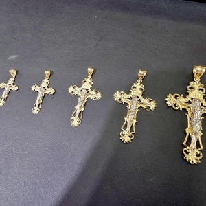 Op de afbeelding: Vijf goudkleurige kruisbeeldhangers van verschillende formaten, elk met een gedetailleerde afbeelding van Jezus Christus. De kruisen hebben sierlijke ontwerpen en worden tegen een donkere achtergrond getoond.