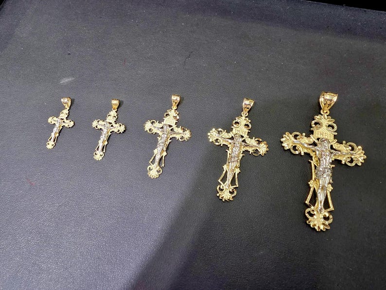 Op de afbeelding: Vijf goudkleurige kruisbeeldhangers van verschillende formaten, elk met een gedetailleerde afbeelding van Jezus Christus. De kruisen hebben sierlijke ontwerpen en worden tegen een donkere achtergrond getoond.