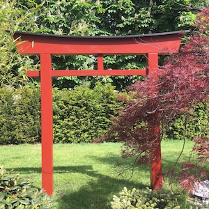 Pu&ograve; includere: Un torii in legno rosso, un tradizionale portale giapponese, si erge in un giardino. Il torii &egrave; fatto di legno e ha una parte superiore nera. Il torii &egrave; circondato da erba verde e alberi.