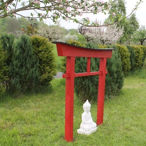 Pu&ograve; includere: Un torii in legno rosso con la parte superiore nera, in piedi in un'area erbosa con una statua bianca di un Buddha in meditazione seduto di fronte ad essa.