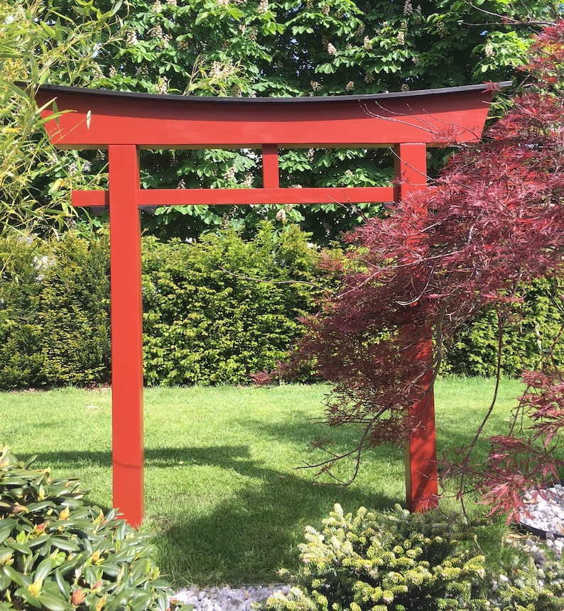 Pu&ograve; includere: Un torii in legno rosso, un tradizionale portale giapponese, si erge in un giardino. Il torii &egrave; fatto di legno e ha una parte superiore nera. Il torii &egrave; circondato da erba verde e alberi.