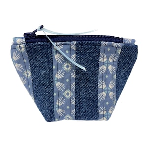 May include: A small, handmade coin purse with a unique design. The purse is constructed from denim and light blue fabric with a floral pattern. It features a dark blue zipper and a light blue ribbon pull. The purse is approximately 5 inches wide.