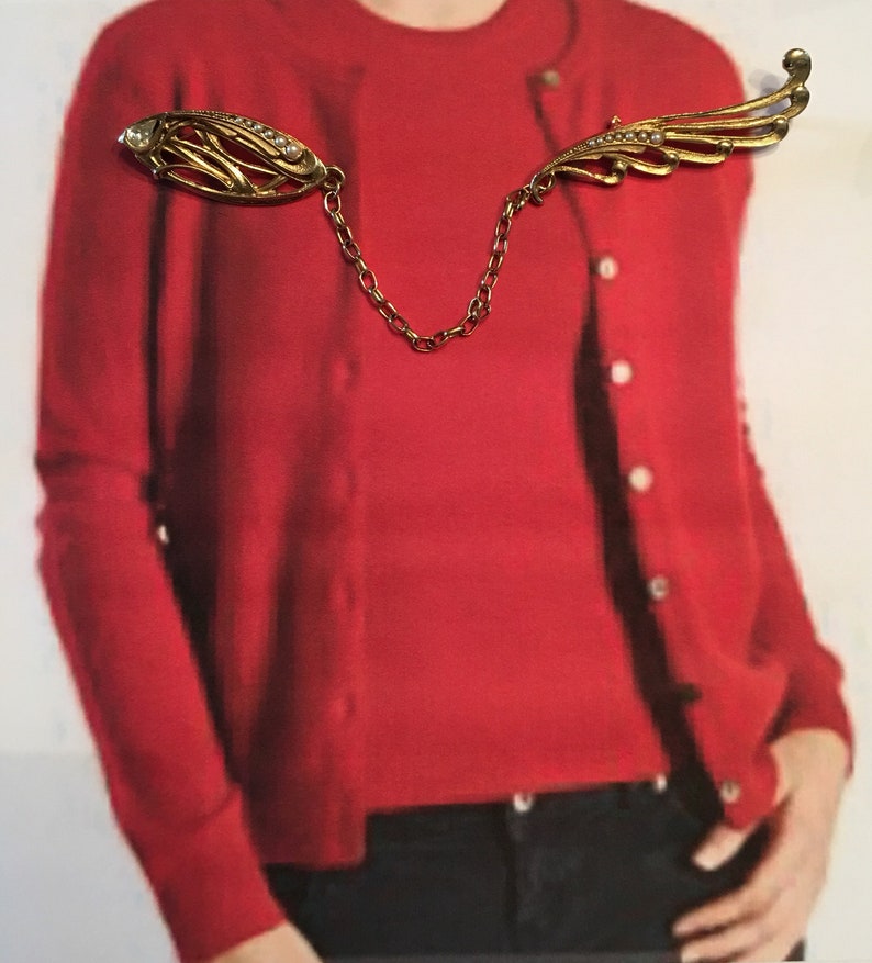 One side is oval seed pearls and rhinestone dramatic sweater pins Vintage gold 4\u201d chain between them the other is a swoosh