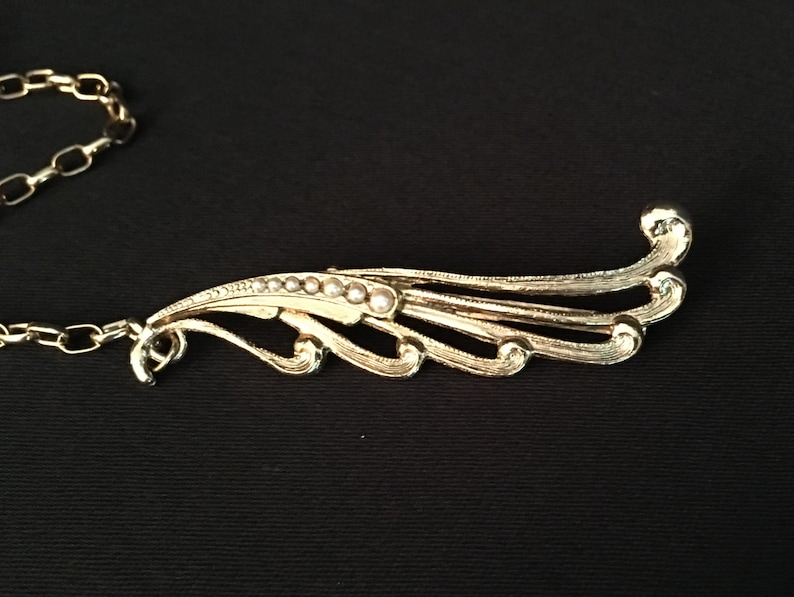 One side is oval seed pearls and rhinestone dramatic sweater pins Vintage gold 4\u201d chain between them the other is a swoosh