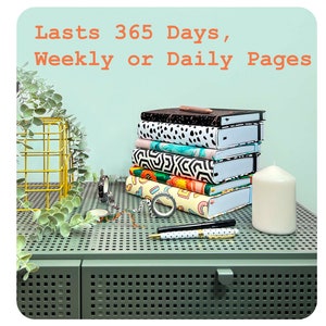 May include: A stack of colourful journals with different patterned covers. The journals are on a green metal surface with a drawer. The text on the top of the image reads "Lasts 365 Days, Weekly or Daily Pages".