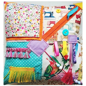 May include: A colorful patchwork pillow with various textures, including fabric, fringe, and sequins. The pillow features a zipper, buttons, and a variety of patterns, including floral, polka dots, and sewing machines.