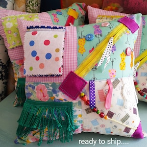 May include: A colourful patchwork cushion with a green fringe, featuring a variety of fabrics, including polka dots, floral patterns, and a zip. The cushion is ready to ship.