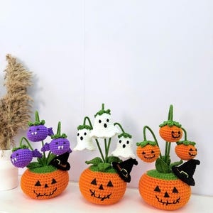 May include: Three crocheted Halloween-themed planters. Each features a round orange pumpkin base with a jack-o'-lantern face. The first holds purple bat-like figures, the second holds white ghost figures, and the third holds orange pumpkin figures.