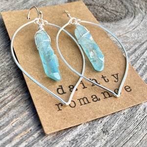 Puede incluir: Aretes de aro de plata con un colgante de cristal azul claro. Los aretes est&aacute;n en una tarjeta marr&oacute;n con el texto "dainty romance".