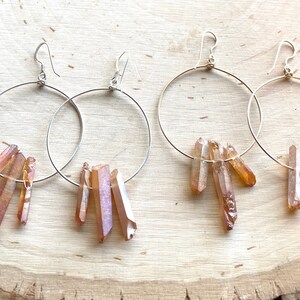 May include: A pair of silver hoop earrings with dangling, raw, peach-colored crystal points.
