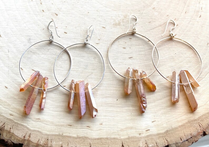 May include: A pair of silver hoop earrings with dangling, raw, peach-colored crystal points.