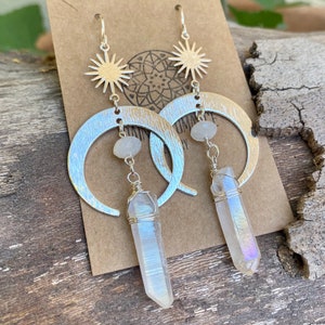 Pu&ograve; includere: Orecchini a forma di mezzaluna d'argento con un ciondolo a stella e un pendente di cristallo bianco iridescente.