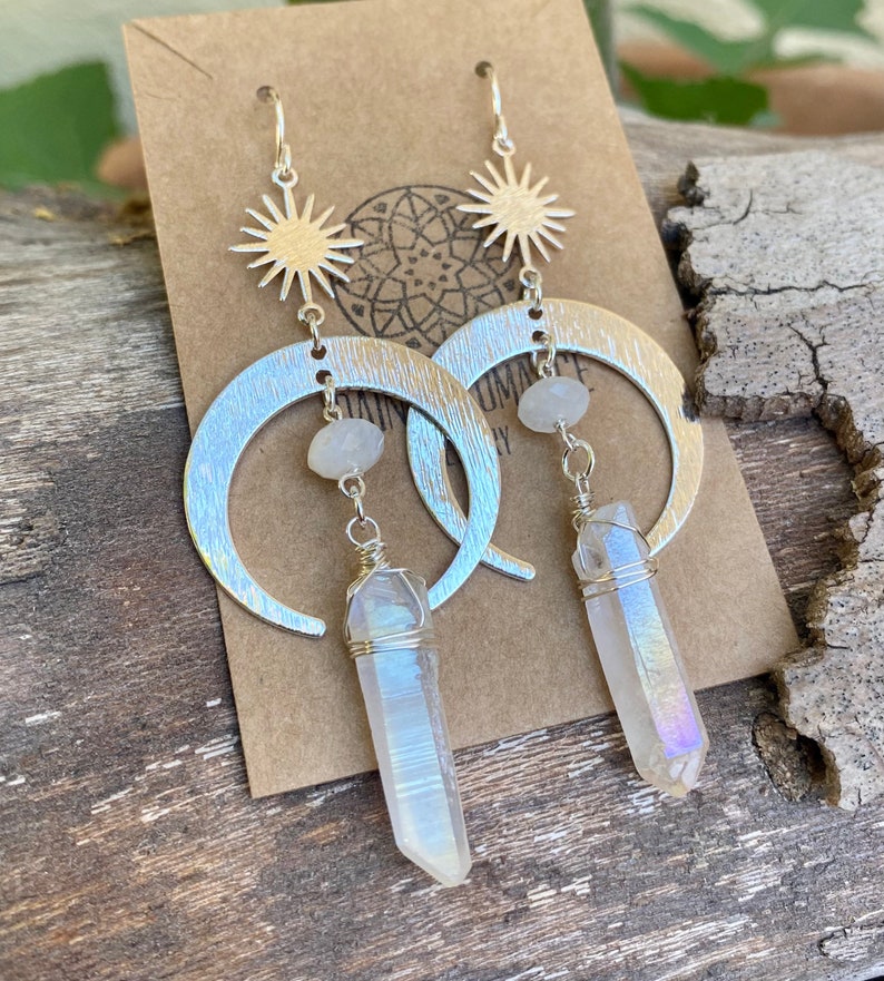 Pu&ograve; includere: Orecchini a forma di mezzaluna d'argento con un ciondolo a stella e un pendente di cristallo bianco iridescente.