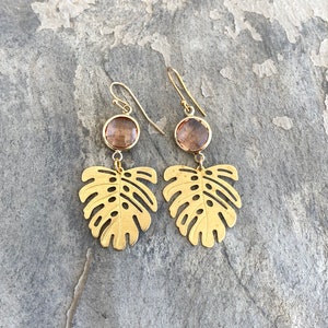 May include: Gold earrings with a brown gemstone and a cutout monstera leaf design.