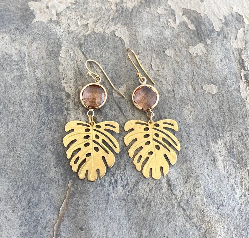 May include: Gold earrings with a brown gemstone and a cutout monstera leaf design.