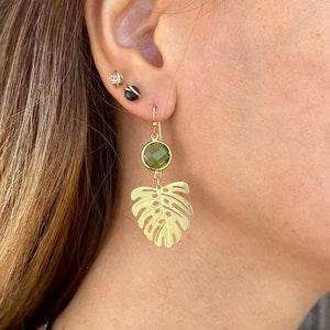 May include: Gold earrings with a green gemstone and a leaf design.