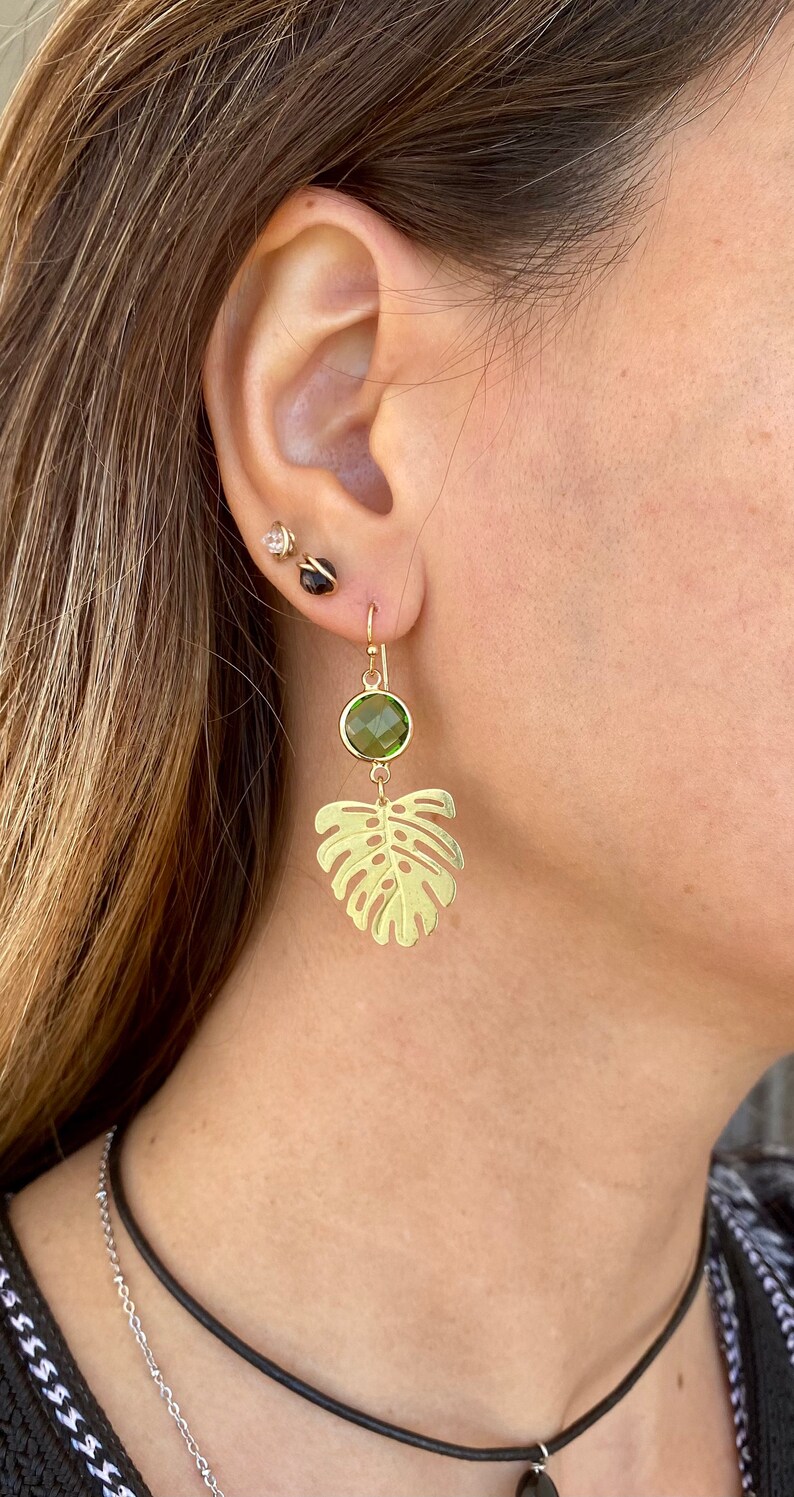 May include: Gold earrings with a green gemstone and a leaf design.