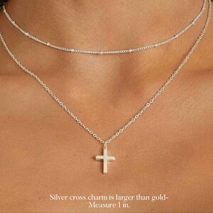 May include: A silver chain necklace with a silver cross charm. The cross charm is larger than the chain links. The necklace is layered over a smaller silver chain necklace with tiny beads.  Silver cross charm is larger than gold - Measure 1 in.