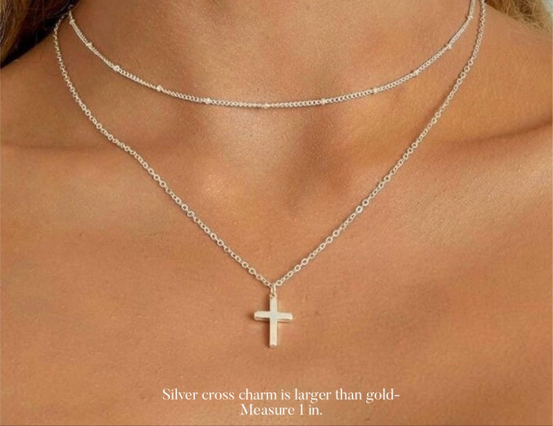 May include: A silver chain necklace with a silver cross charm. The cross charm is larger than the chain links. The necklace is layered over a smaller silver chain necklace with tiny beads.  Silver cross charm is larger than gold - Measure 1 in.