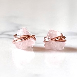 Può includere: Un paio di orecchini in quarzo rosa con filo avvolto in oro rosa. Gli orecchini sono di colore rosa chiaro e hanno una forma naturale irregolare.