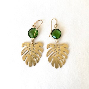 May include: Gold earrings with green gemstone accents and a cutout monstera leaf design.