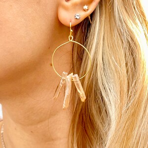 May include: Gold hoop earrings with a cluster of light brown crystal points dangling from the bottom.