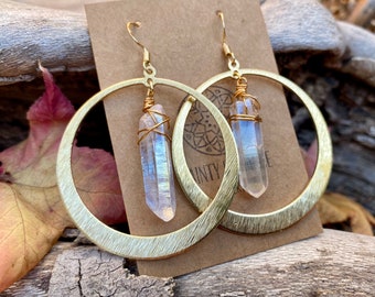 Pode incluir: Brincos de argola de ouro com um cristal de quartzo transparente pendurado em cada argola. As argolas são de ouro escovado e têm uma textura martelada.