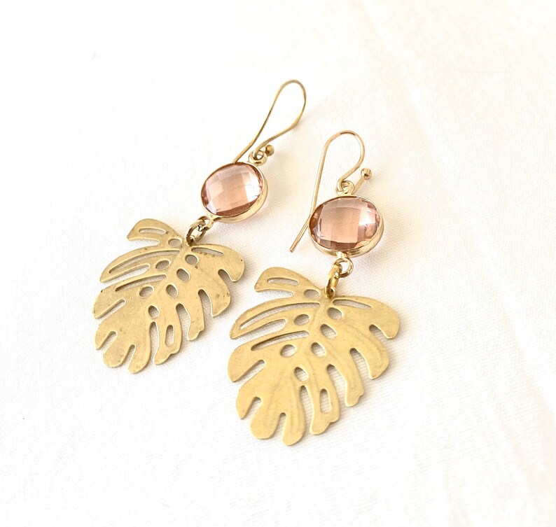 May include: Gold earrings with a pink gemstone and a cutout leaf design.