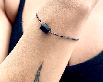 Peut inclure: Un bracelet en chaîne noire avec un seul charme rectangulaire en pierre noire.
