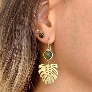 May include: Gold earrings with a green gemstone and a leaf design.