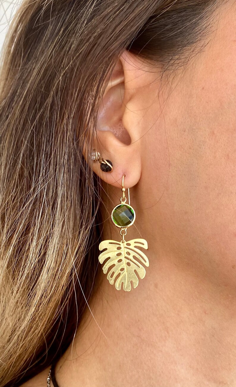 May include: Gold earrings with a green gemstone and a leaf design.