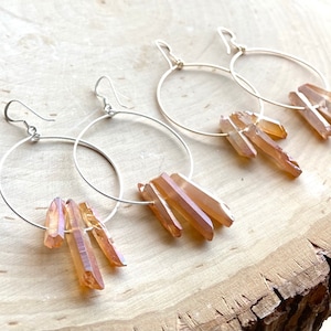 May include: A pair of silver hoop earrings with a cluster of light brown crystal points dangling from each hoop.