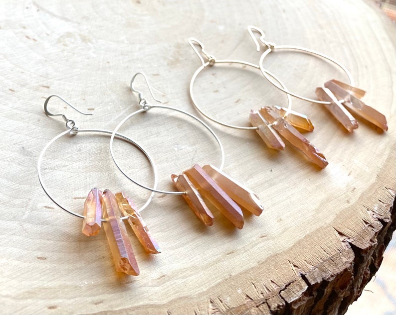 May include: A pair of silver hoop earrings with a cluster of light brown crystal points dangling from each hoop.