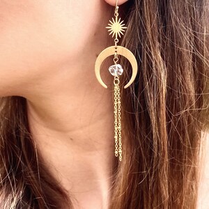 May include: Gold crescent moon earrings with a star charm and a crystal bead dangling from a chain.