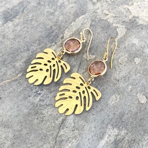 May include: Gold earrings with a leaf design and a pink gemstone dangle. The earrings are made of metal and have a delicate, feminine look.