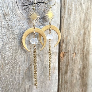 May include: Gold crescent moon earrings with a small clear crystal and a gold sun charm dangling from each earring. The earrings have a delicate gold chain that hangs below the crystal.
