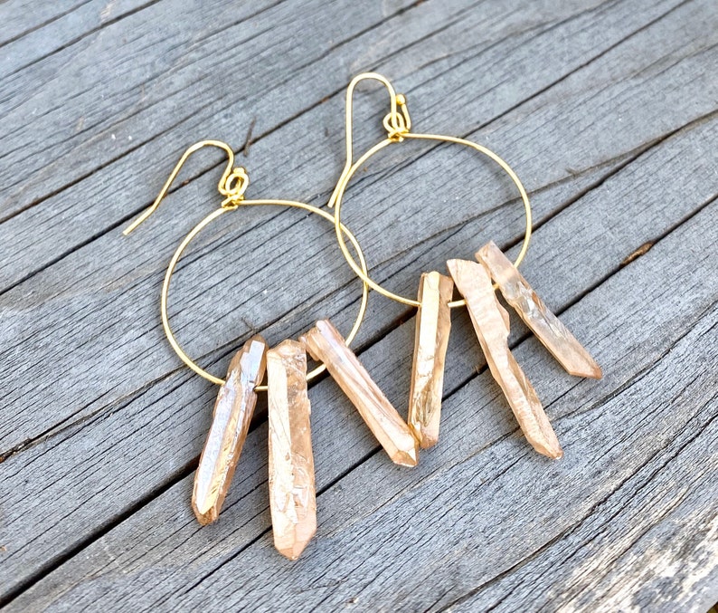 May include: Gold hoop earrings with a cluster of light brown crystal points dangling from each hoop.