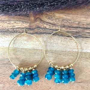 May include: Gold hoop earrings with a dangling cluster of turquoise blue gemstone beads.