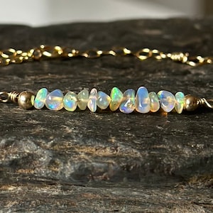 May include: A delicate gold chain bracelet with a row of iridescent white opal chips.