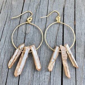 May include: Gold hoop earrings with three clear quartz crystal points dangling from each hoop.