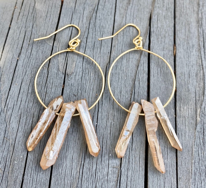May include: Gold hoop earrings with three clear quartz crystal points dangling from each hoop.