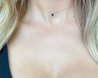 Può includere: Una delicata collana a catena dorata con un piccolo ciondolo di pietra nera.