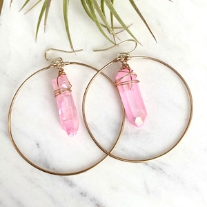 Puede incluir: Un par de pendientes de aro dorados con colgantes de cristal rosa. Los cristales est&aacute;n envueltos en alambre dorado.