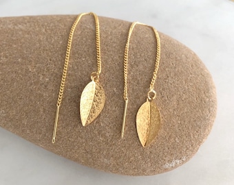 May include: A pair of gold leaf dangle earrings with a delicate chain. The earrings are made of gold-plated metal and feature a textured leaf design.