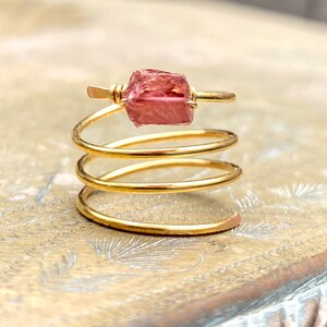 May include: A gold wire ring with a pink gemstone wrapped around the band.