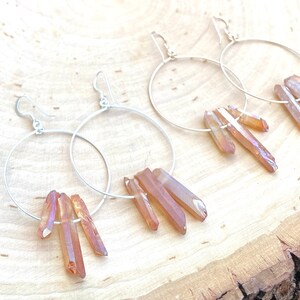 May include: A pair of silver hoop earrings with dangling iridescent orange crystal points.